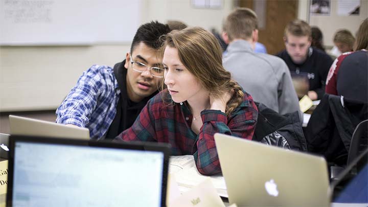 Two students at a laptop discussing a problem.