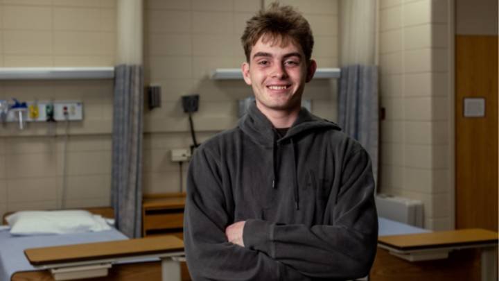 A male college student smiling wearing a sweatshirt in a hospital setting.