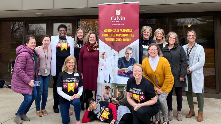 A group of 13 women stand near a pop-up sign for the School of Health.