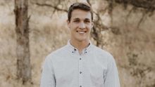 A headshot of Nick Moll smiling in a button down shirt standing outside.