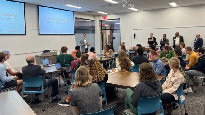 A classroom of students and trustees listen to a speaker present.