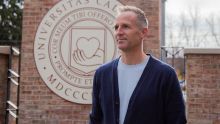 A professor stands in front of university signage staring off into the distance