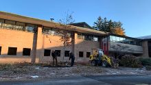 Two Calvin staff members plant an oak tree on campus in front of a building.