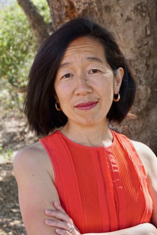 Felicia, an Asian woman, with shoulder-length black hair and small gold hoop earrings, stands with her arms crossed, wearing a red short-sleeve dress in front of a tree.