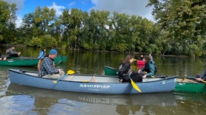 A few canoes with two people in each floating down a river.