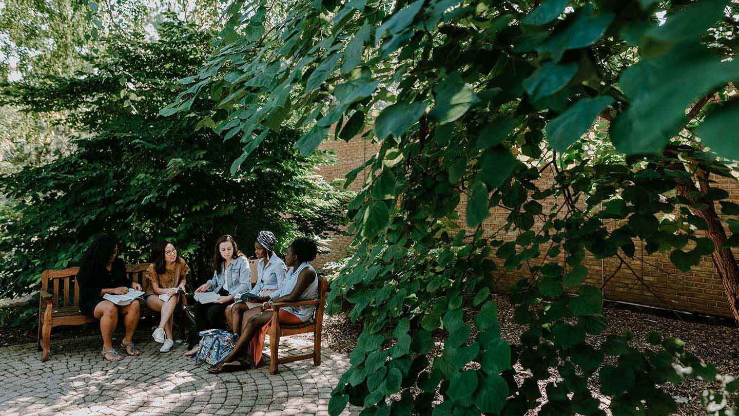 Students sitting, conversing on benches outside library lobby