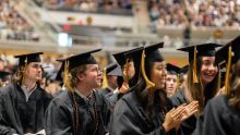 Students in black caps and gowns watching at their graduation ceremony.