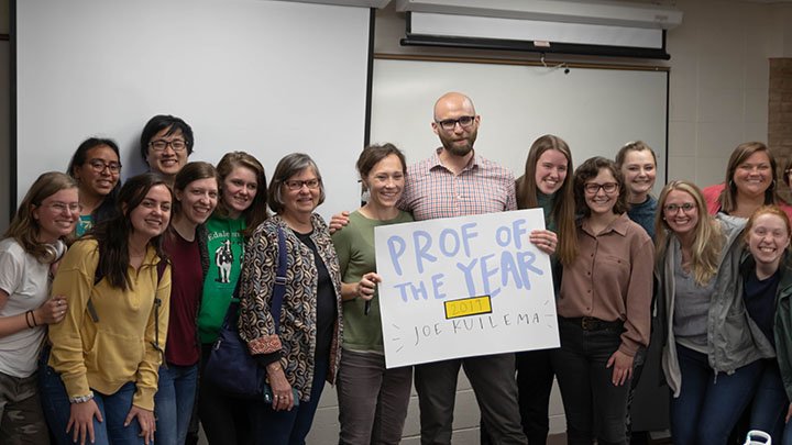 A professor holds a sign that says 