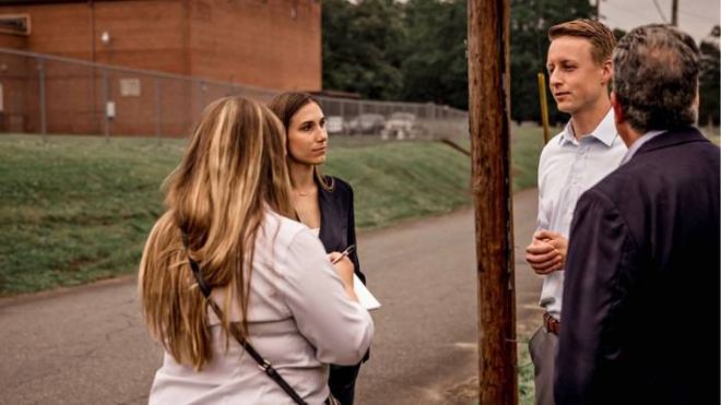 A reporter with a notepad interviews Noah Praamsa and two of his colleagues outdoors.