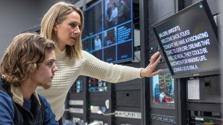 Jessica Harthorn points at a teleprompter as a student looks on.