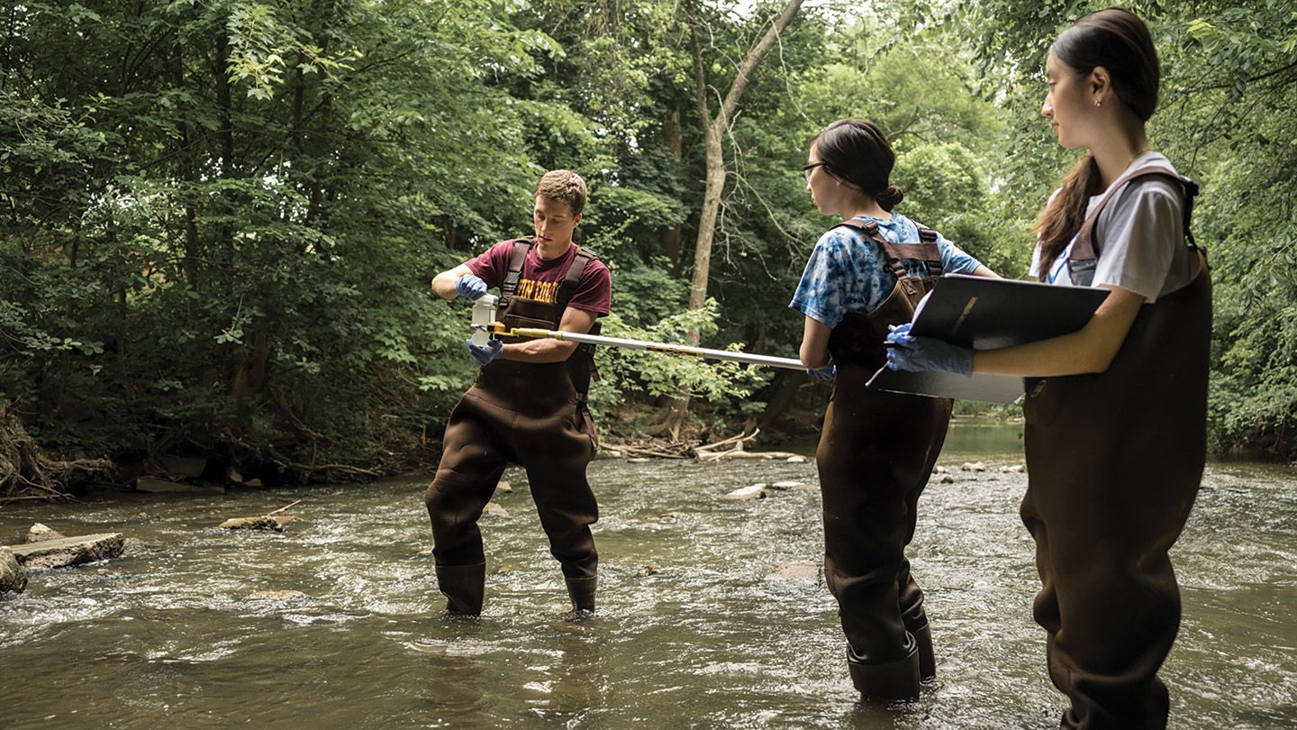 Calvin professor demonstrates to students a water sample he's holding, in Plaster Creek.