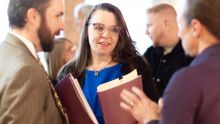 A woman wearing glasses interacts with a couple of people in a lobby following her plenary address.