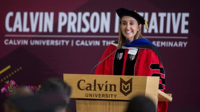 A Calvin administrator dressed in red regalia stands behind a podium.