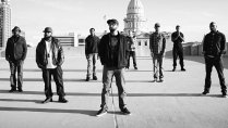 Rappers from AOTA stand, dispersed on a building, looking at the screen.