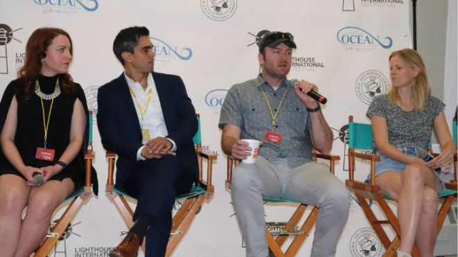 Four panelists sit in director's chairs, one holding a microphone.