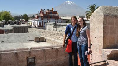 Two students smile in front of a stone wall in a foreign city.