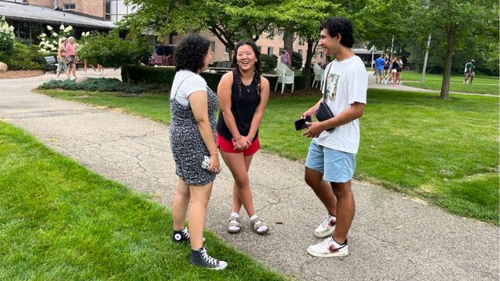 Two female and one male college student talk on a walkway on Calvin University's campus.