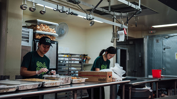 Two students in a kitchen package up unused food to distribute to a local food bank.