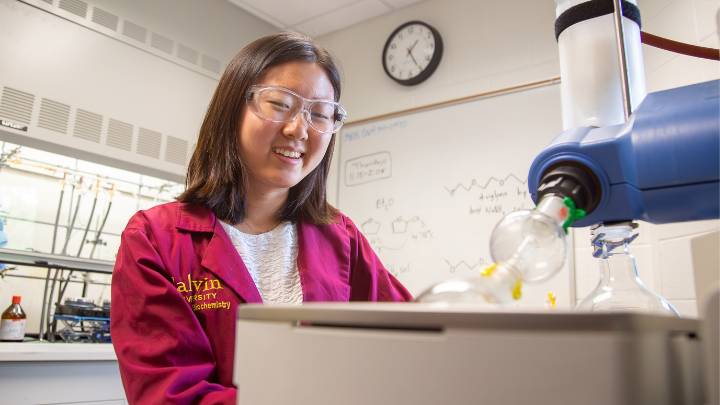 A student smiles as she performs research in a lab at Calvin University.