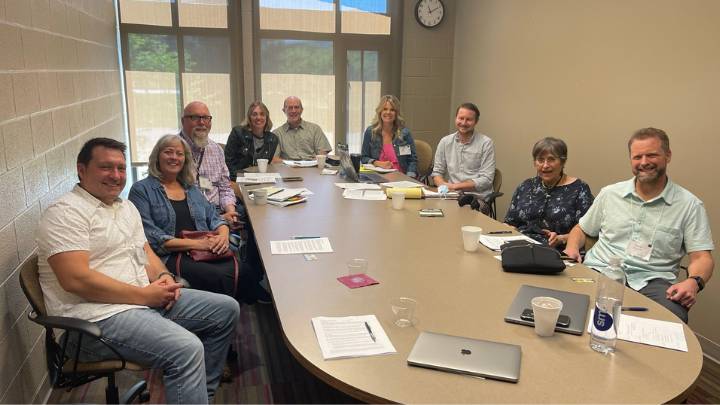 Nine people sitting around a table with writing samples in front of them smile at the camera.