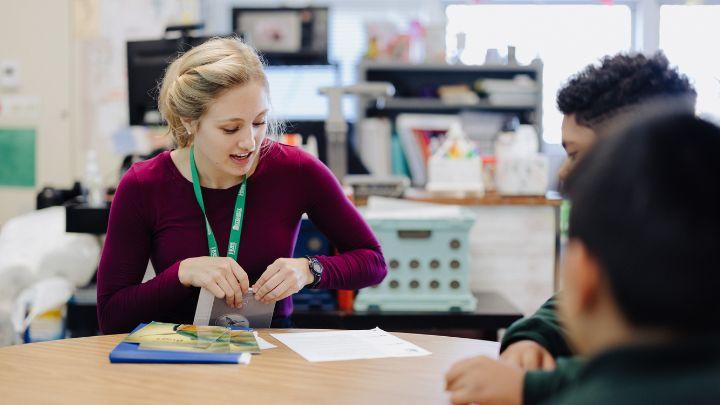 A young woman sitting at a table student teaching with kids.