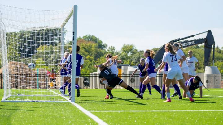 Women's soccer playing game on new turf field with construction equipment in the background.